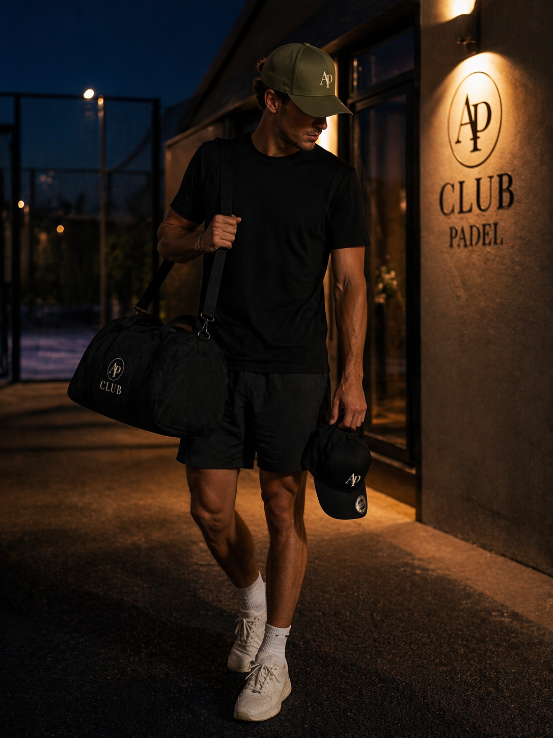 Man walking outside a padel club building with 'Club Padel' branding, holding a black AP Club duffel bag and AP Club cap.