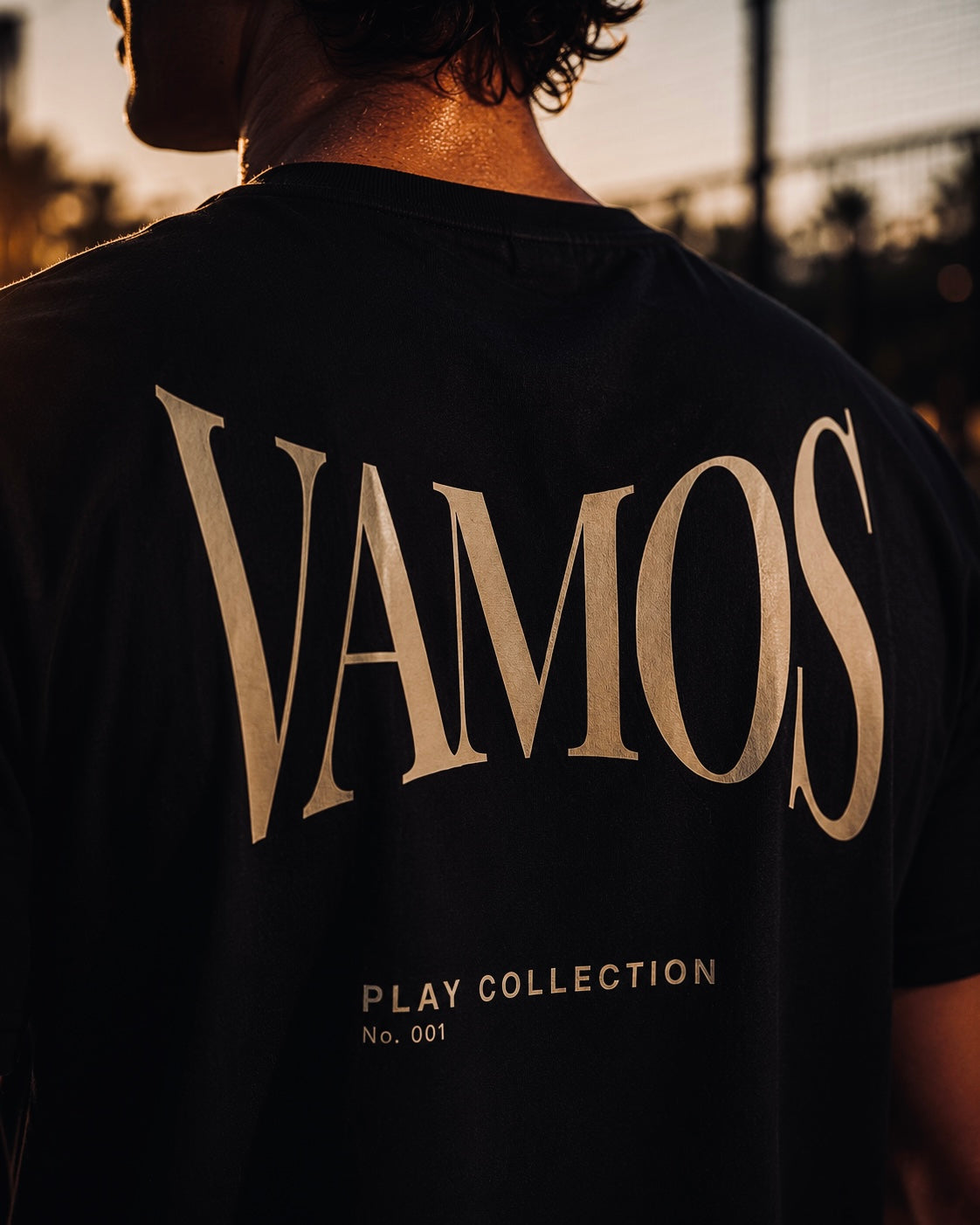 AP Club Vamos Tee (Play Collection No.001) – close-up back view of black t-shirt with gold 'VAMOS' graphic, British padel apparel.