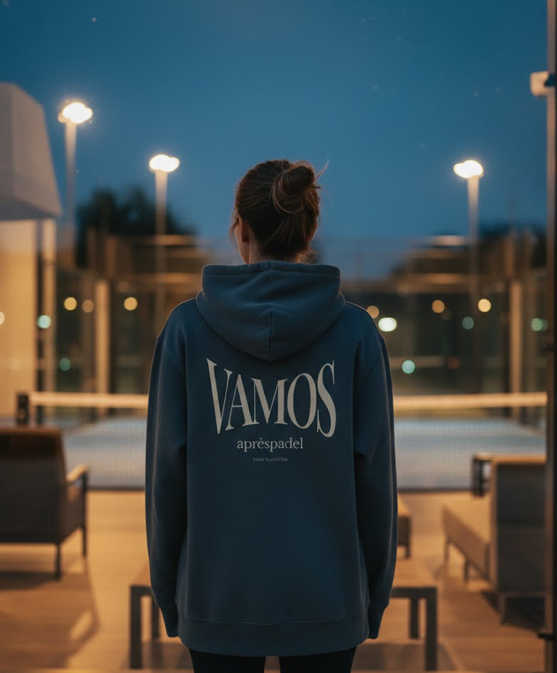 Person wearing a grey AP Club Vamos hoodie with 'VAMOS' text standing in an outdoor padel court at night.