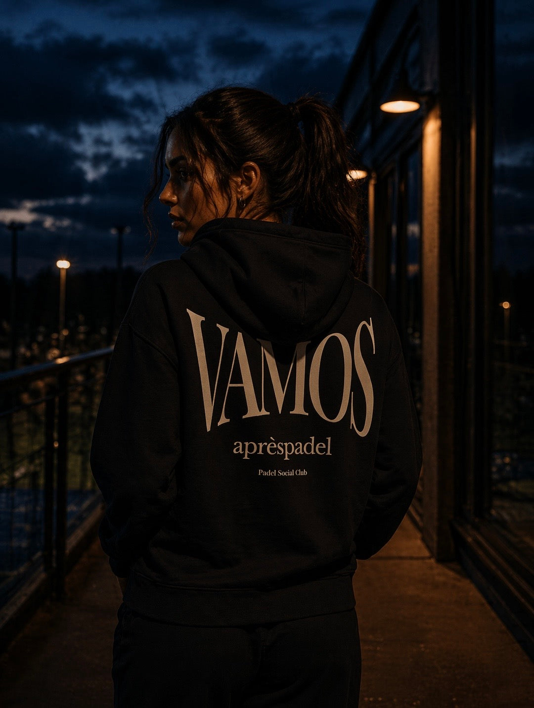Female padel player wearing a black AP Club hoodie with 'VAMOS aprèspadel' text at night.