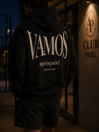 Person wearing a black AP Club Vamos hoodie with 'VAMOS' text, standing in front of a building with 'Club Padel' sign.