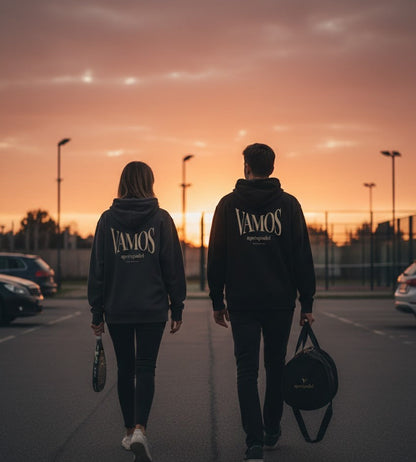 Two people walking to a padel court at sunset, wearing AP Club VAMOS hoodies.